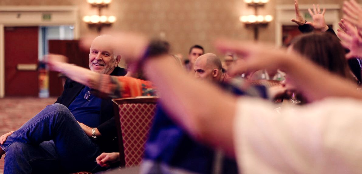A corporate audience with hands raised, taking part in Eric Lerner's stage show