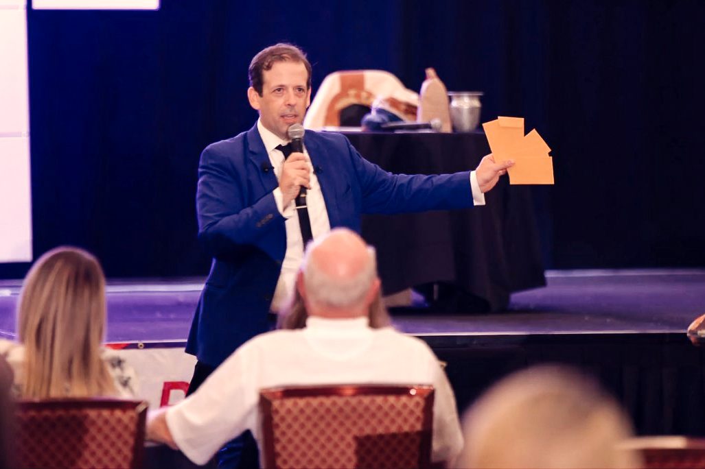 Eric Lerner holding envelopes during a corporate stage show as a seated audience watches