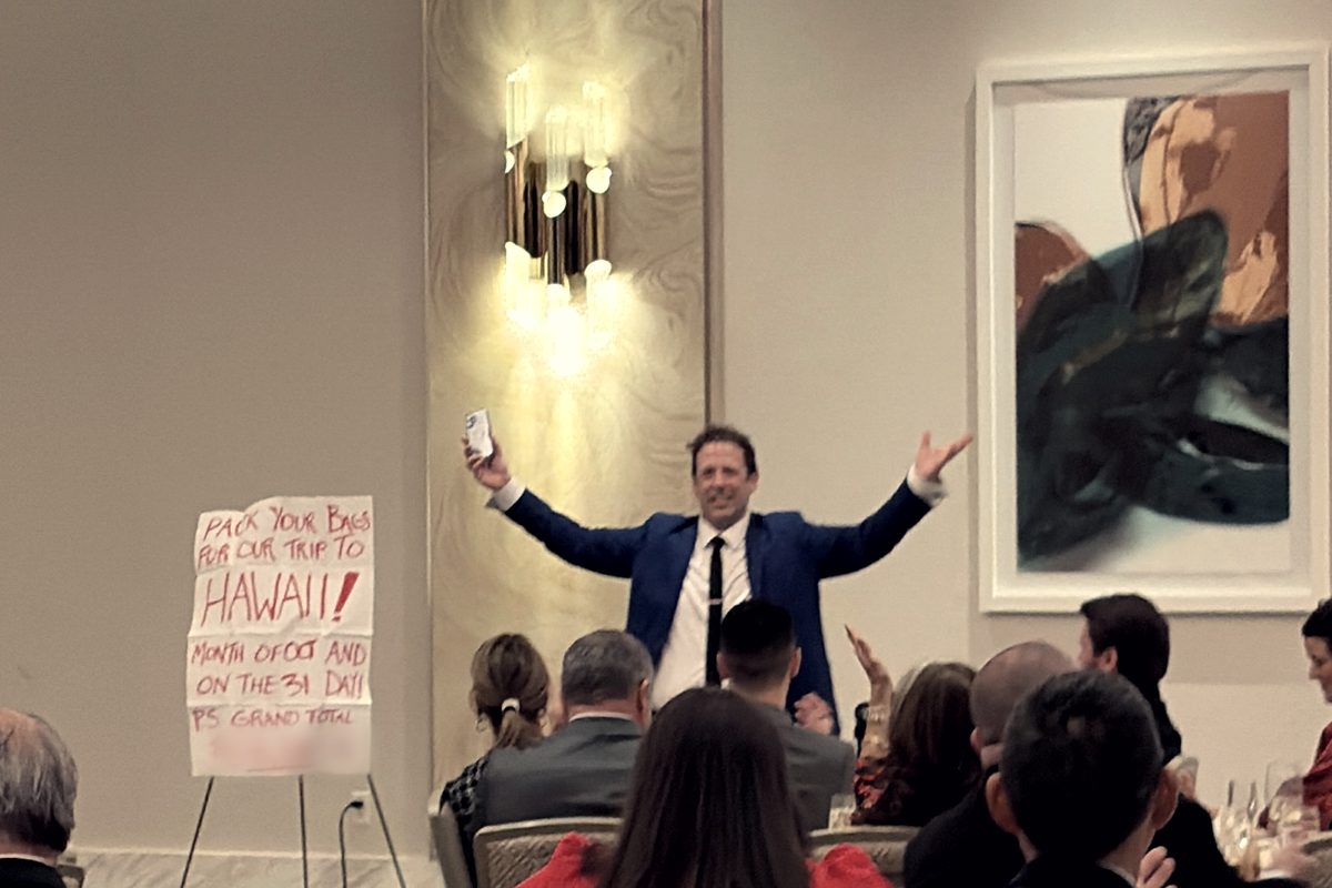 Eric Lerner with his arms open beside a revealed prediction on an easel, at a corporate dinner in a hotel ballroom